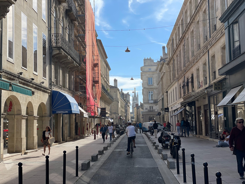 Straße in Bordeaux mit Radfahrer, hellen Fassaden und Geschäften