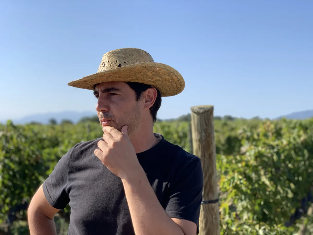 Mann mit Strohhut steht nachdenklich vor Weinreben im Weingut La Vinyeta
