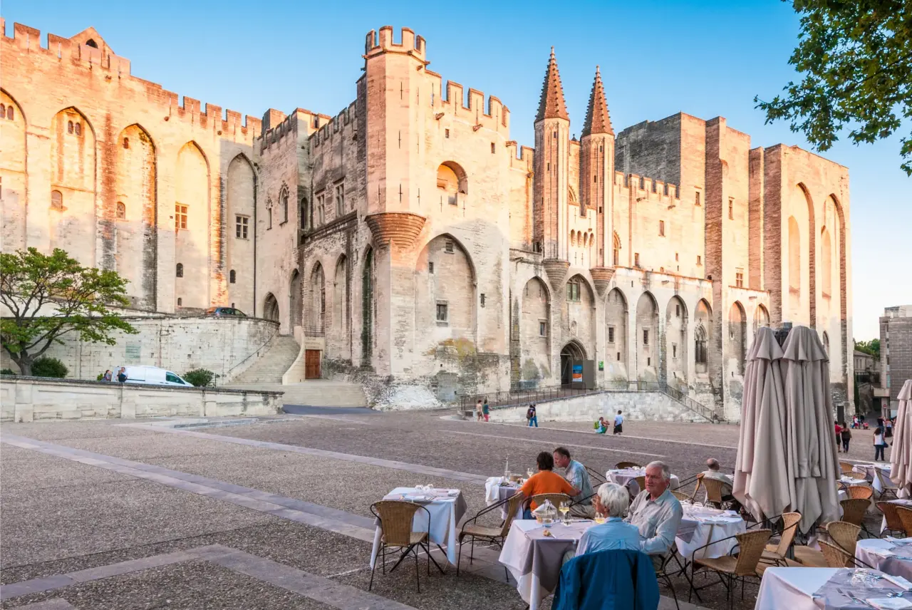 Papstpalast in Avignon im Abendlicht mit Restaurantterrasse davor